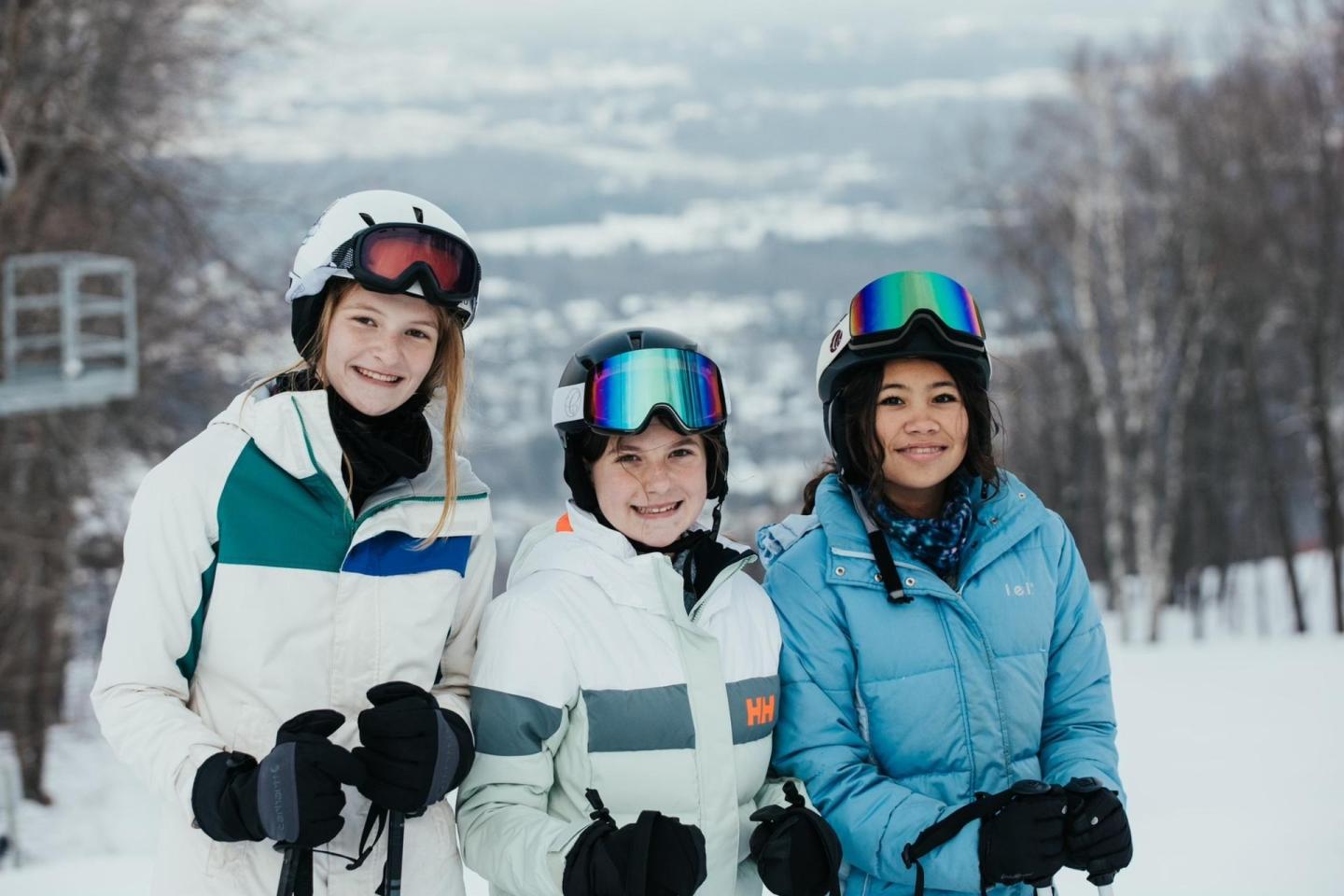 Three smiling people wearing ski gear on a snowy slope.