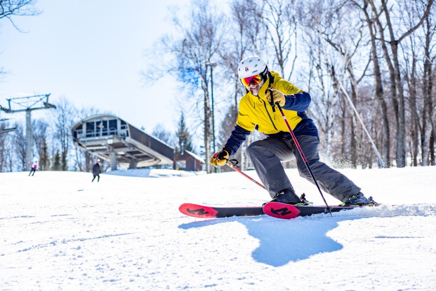 Skier in yellow jacket carving down snowy slope under bright blue sky.