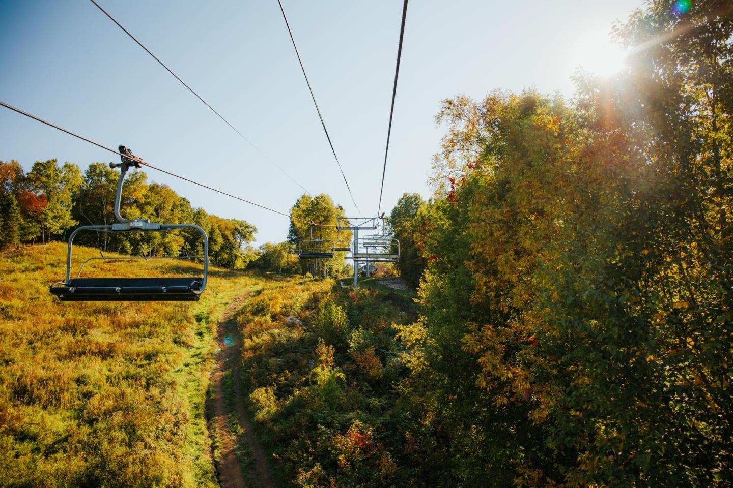 Ski lift over autumn trees and grassy slope under the bright sun.