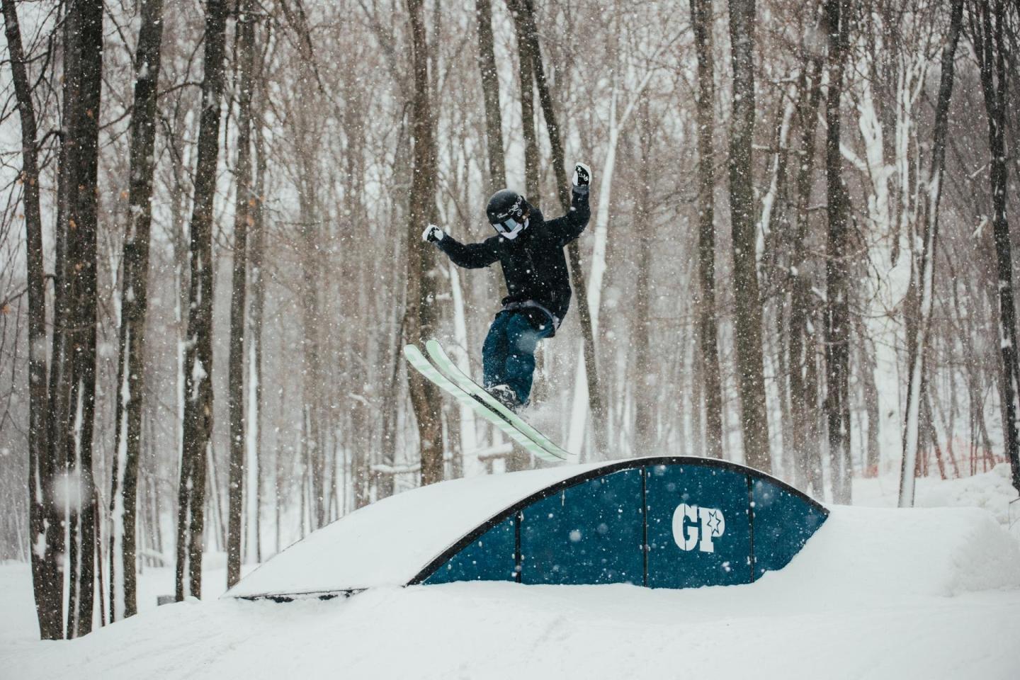 Snowboarder jumping off a ramp in snowy forest.
