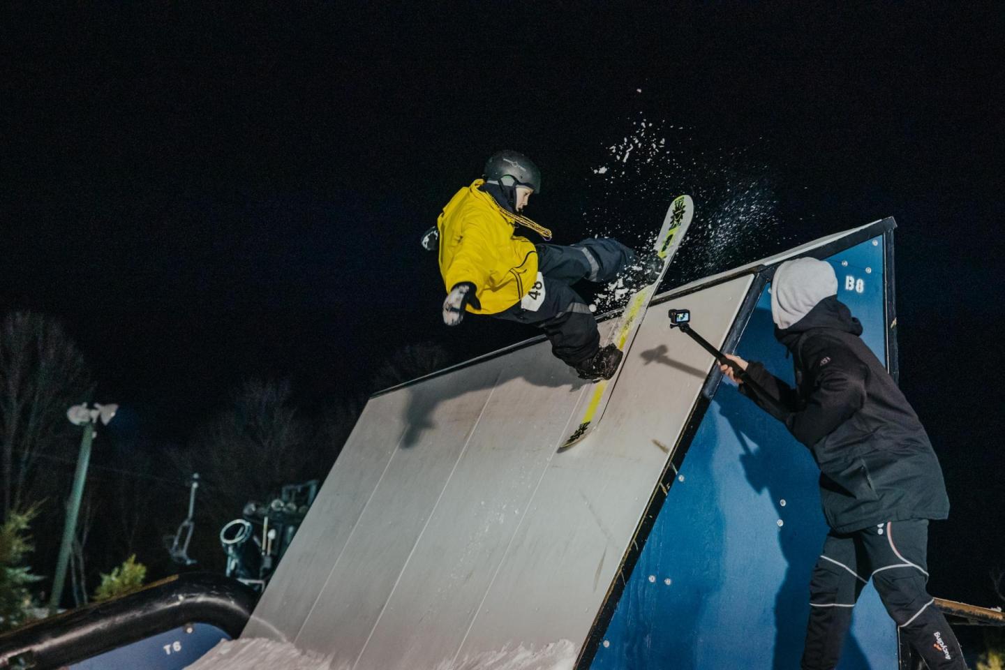Snowboarder in mid-air at night, performing a trick on a ramp.