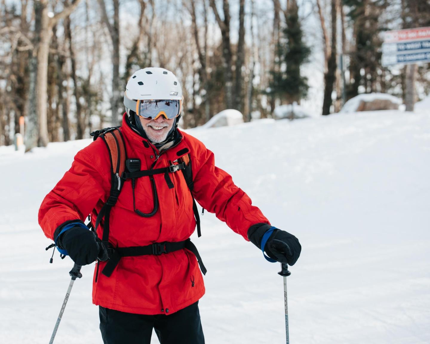 Skier in red jacket and helmet on a snowy slope, trees in the background.