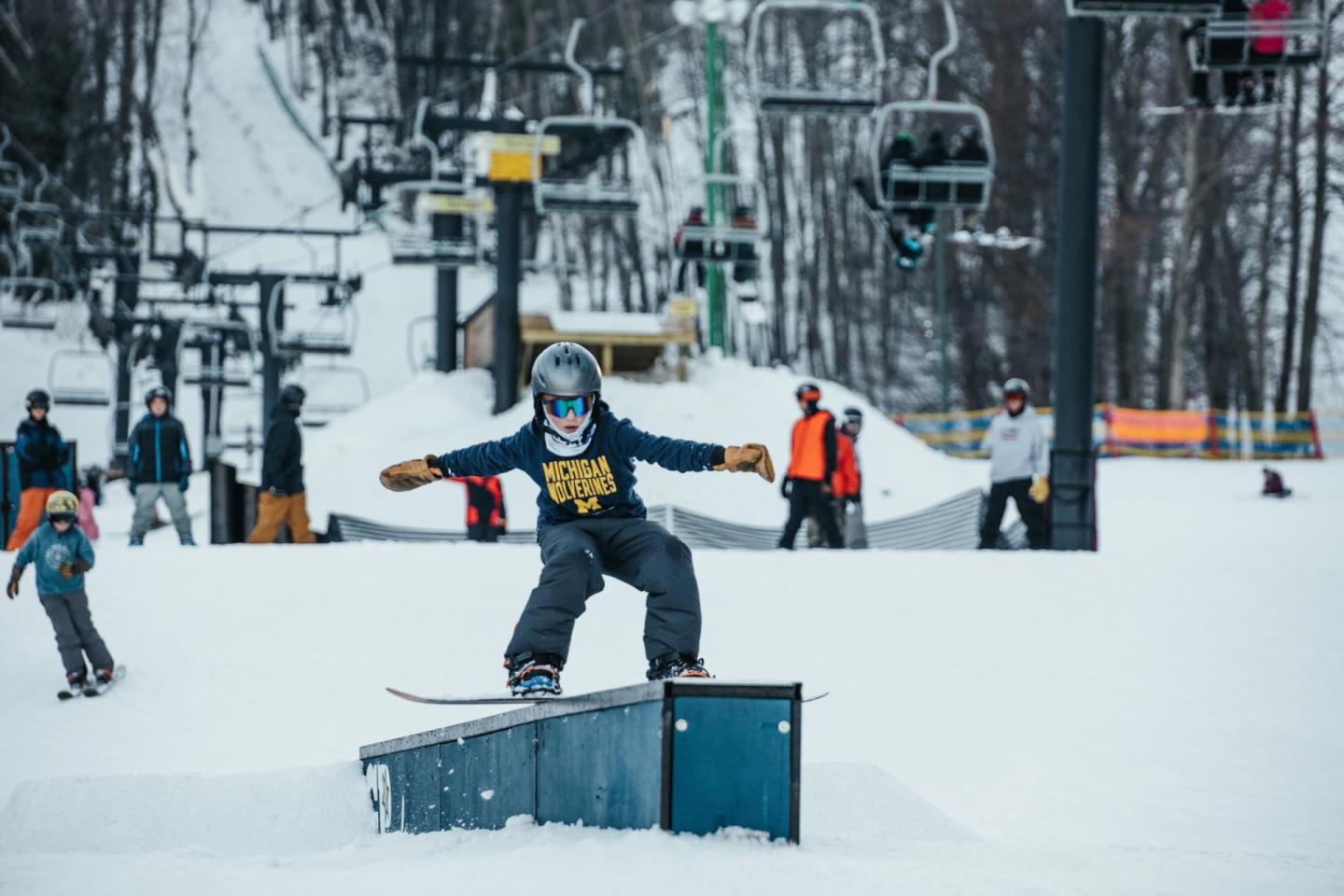 Snowboarder in mid-trick on rail, snowy ski resort background.