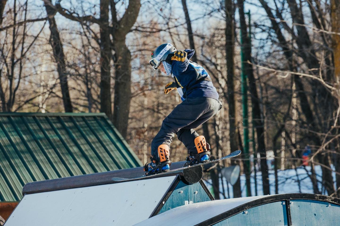 Snowboarder grinding a rail in a snowy, wooded area.