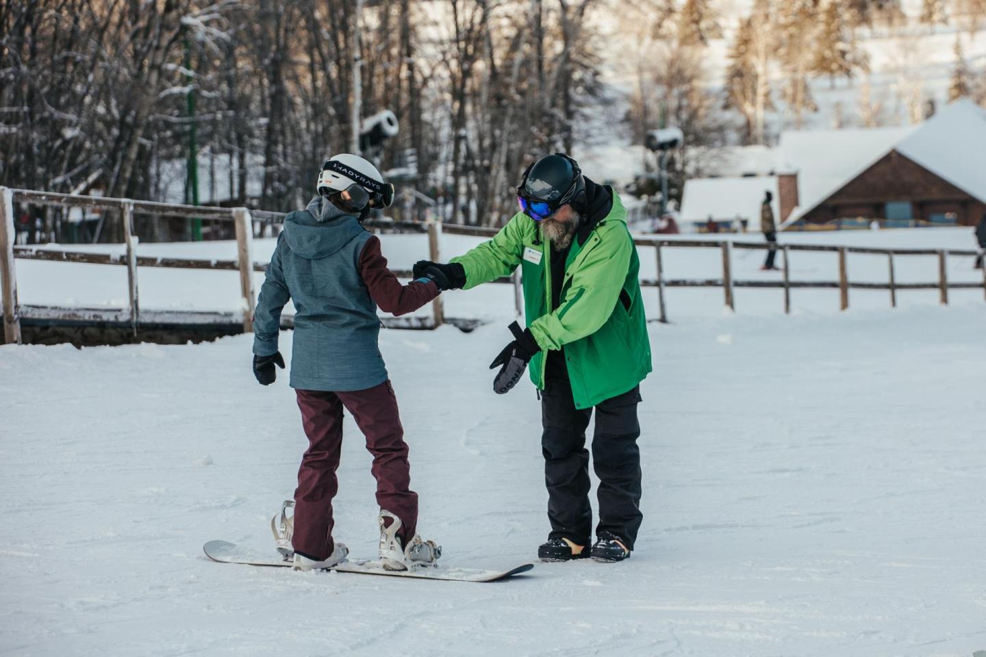 Snowboard lesson; instructor assists a learner on a snowy slope.