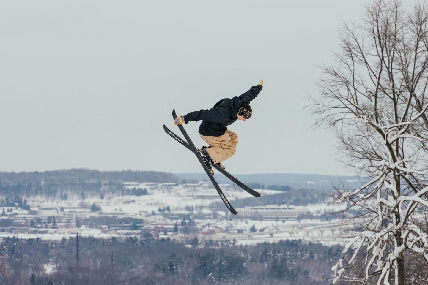 Skier in mid-air trick against snowy landscape backdrop.