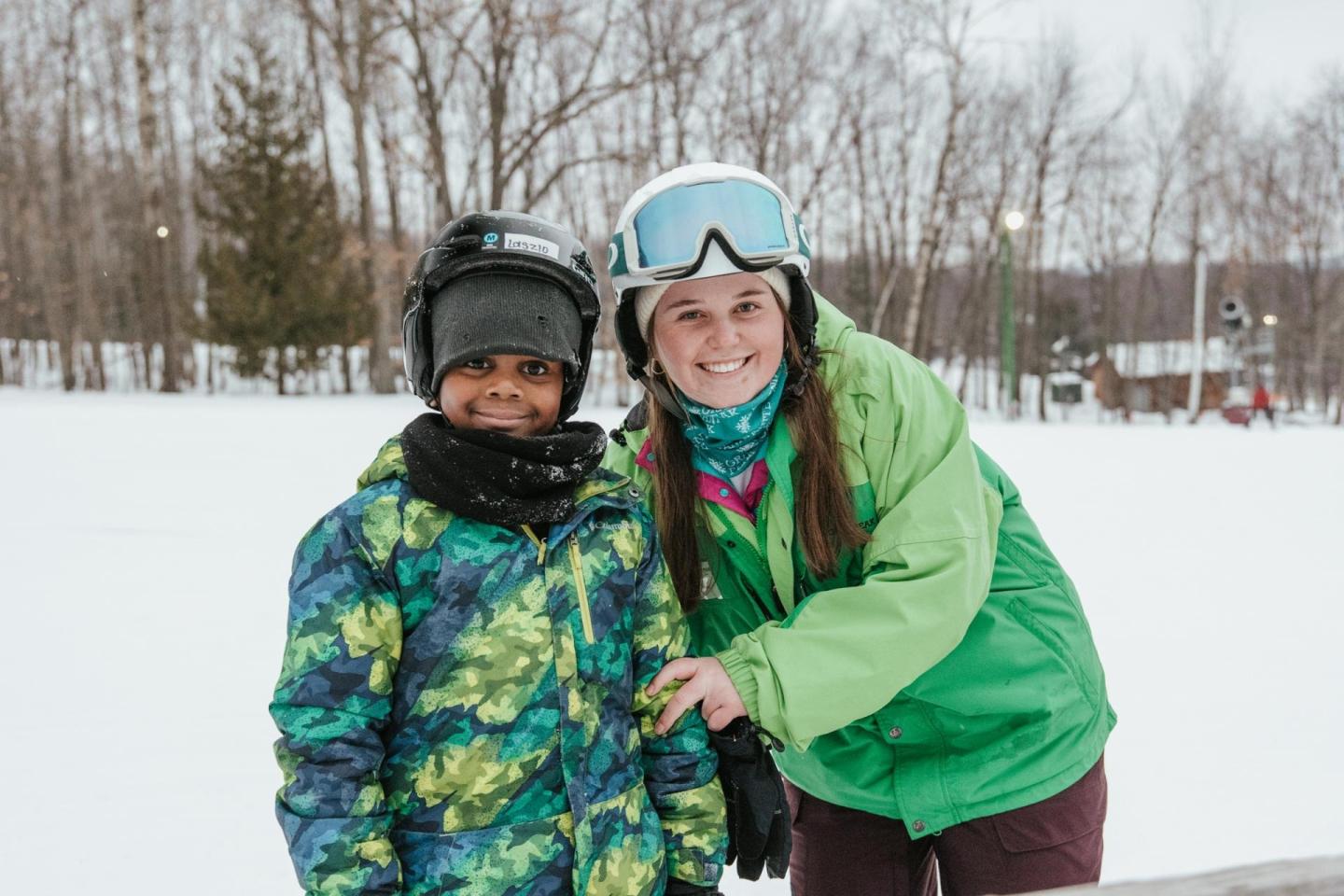 Two smiling people in winter gear on a snowy landscape.