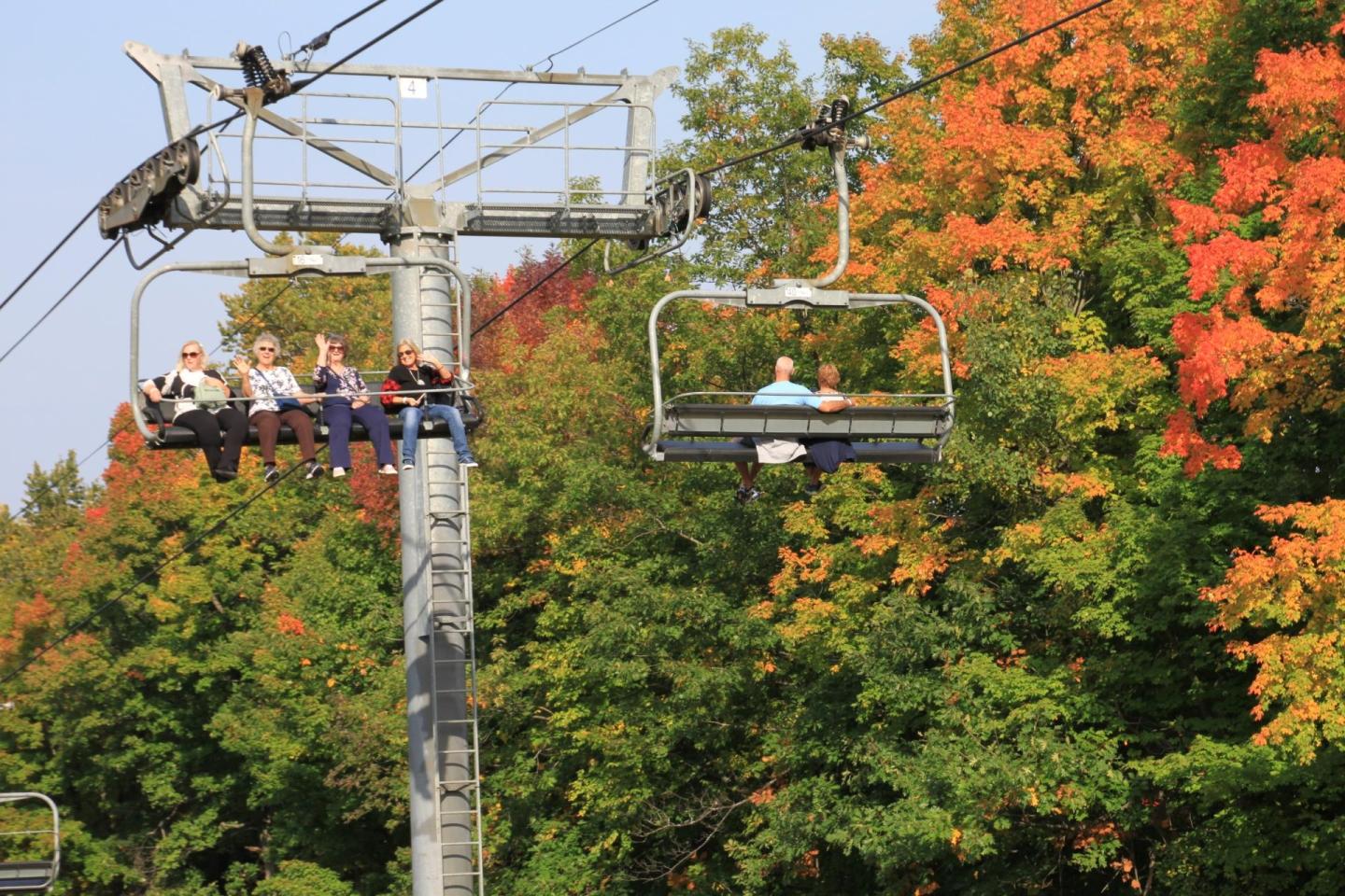 Ski lift with people, surrounded by vibrant autumn trees.