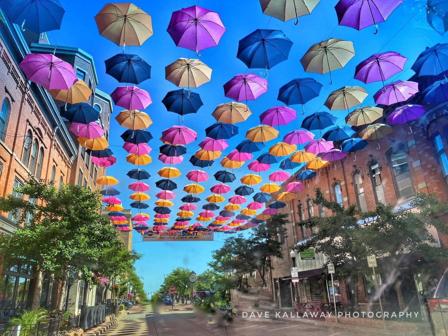 Colorful umbrellas suspended over a street with brick buildings.