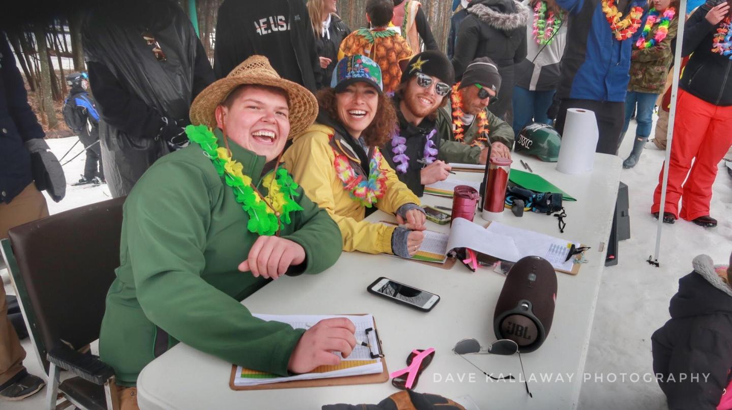 Judges in colorful attire laughing at an outdoor event table.