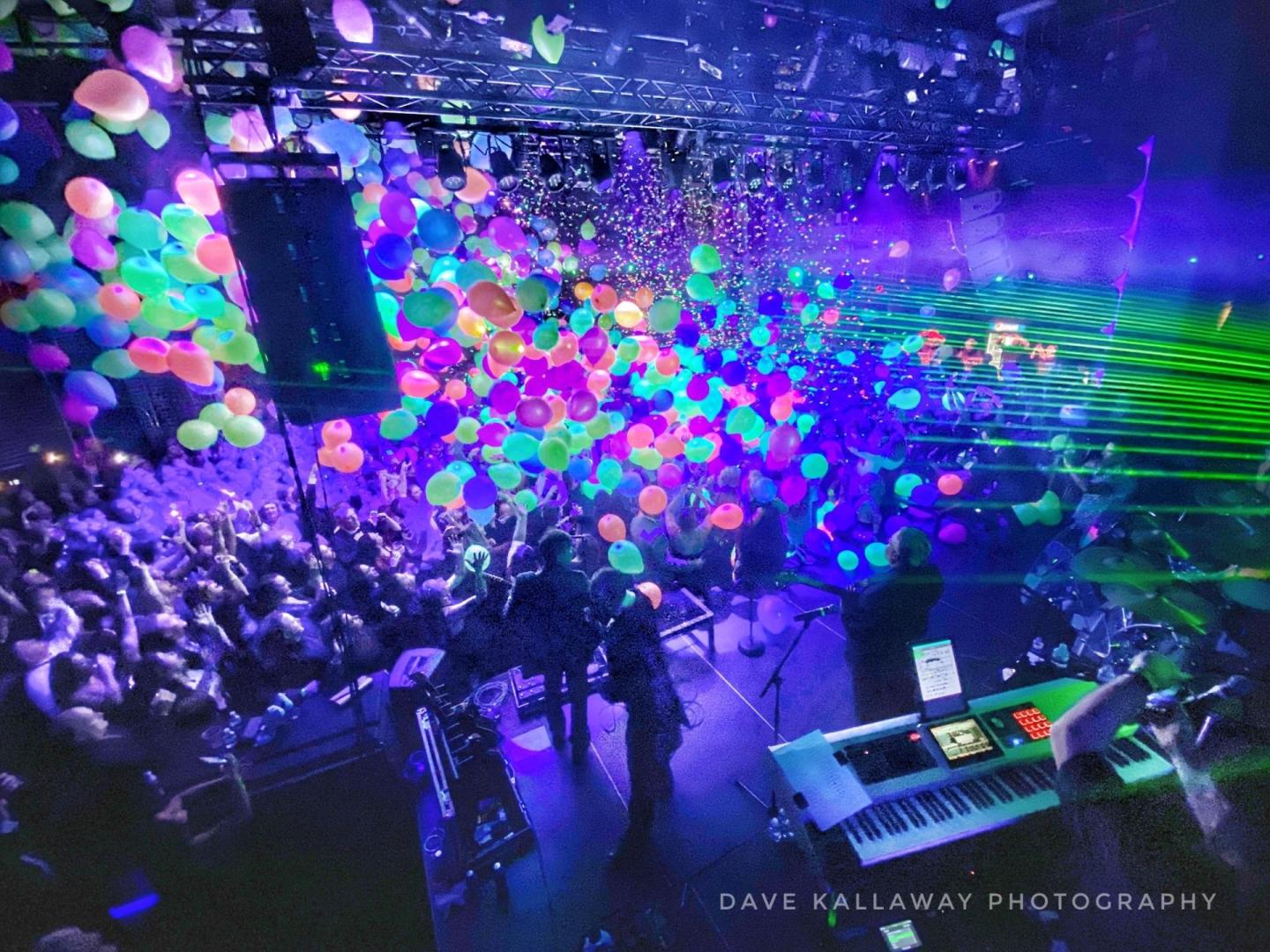 Concert with colorful balloons, stage lights, and a lively crowd.