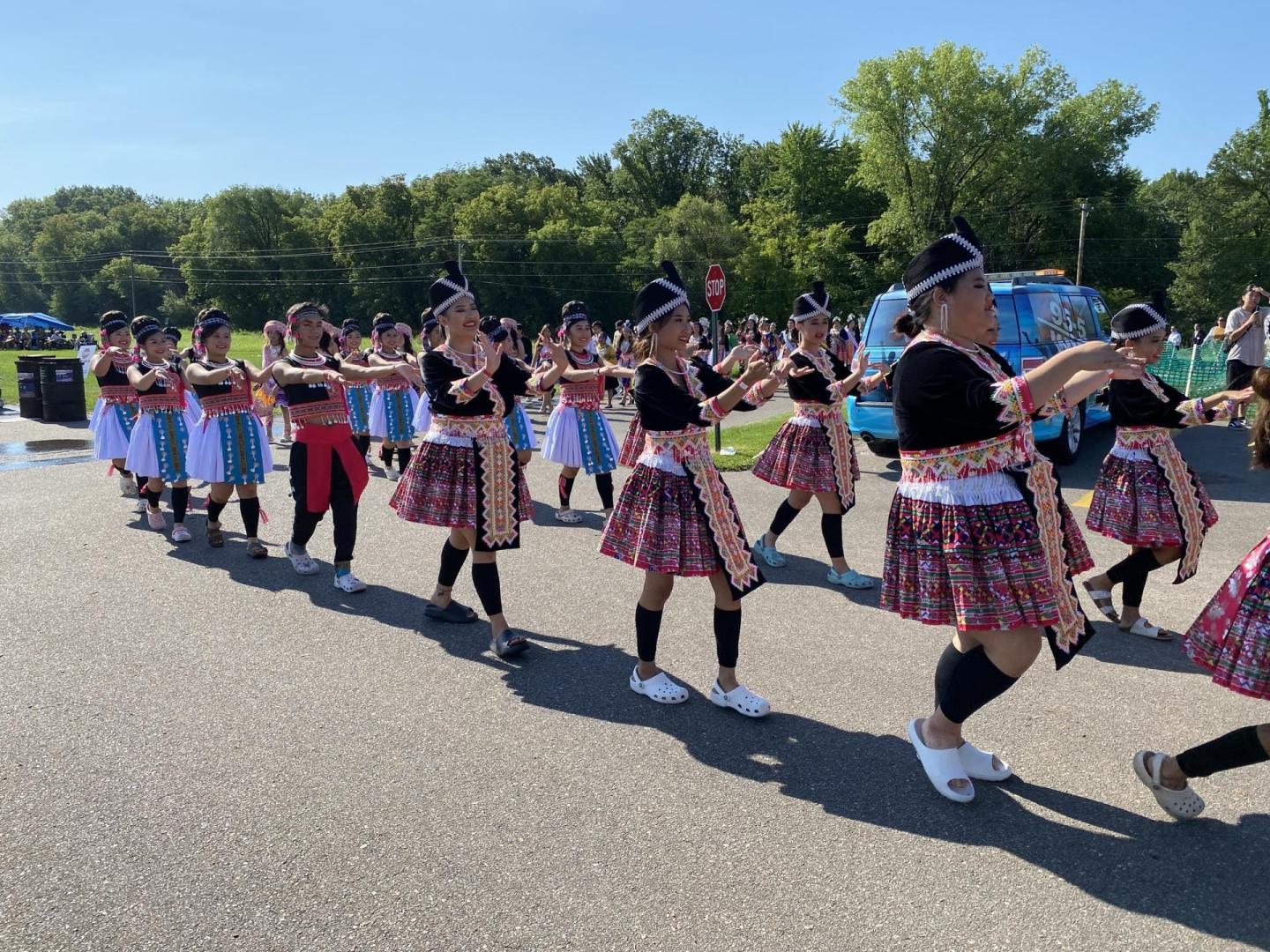 Dancers in traditional attire performing outdoors in a sunny park.