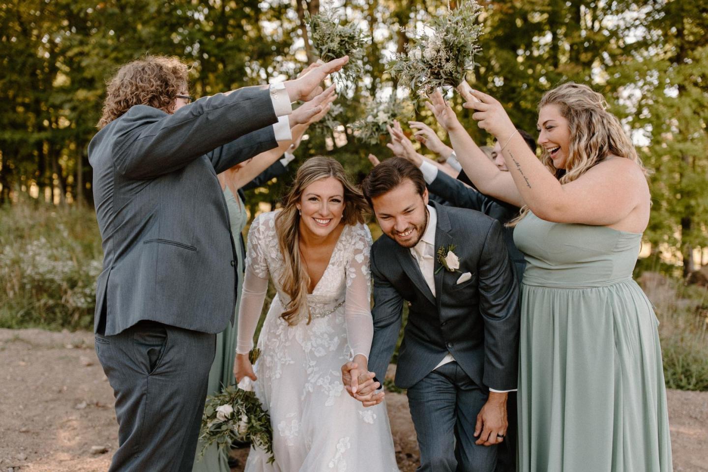 Bride and groom smiling under a flower arch made by bridesmaids and groomsmen.