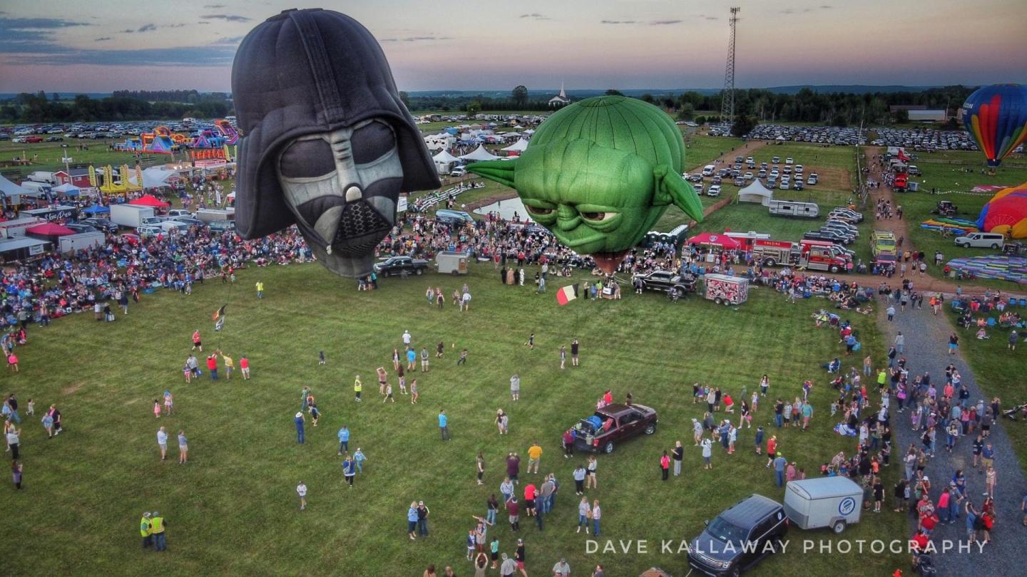 Hot air balloons shaped like helmets at a festival crowd.