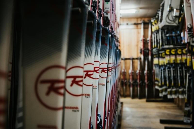 Ski equipment lined up in a storage room with wooden walls.