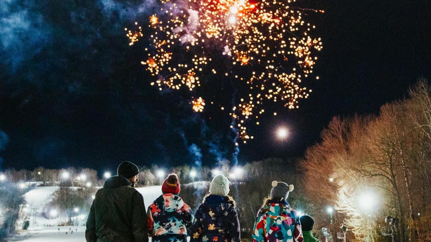 Fireworks explode in the night sky above people in winter clothing.