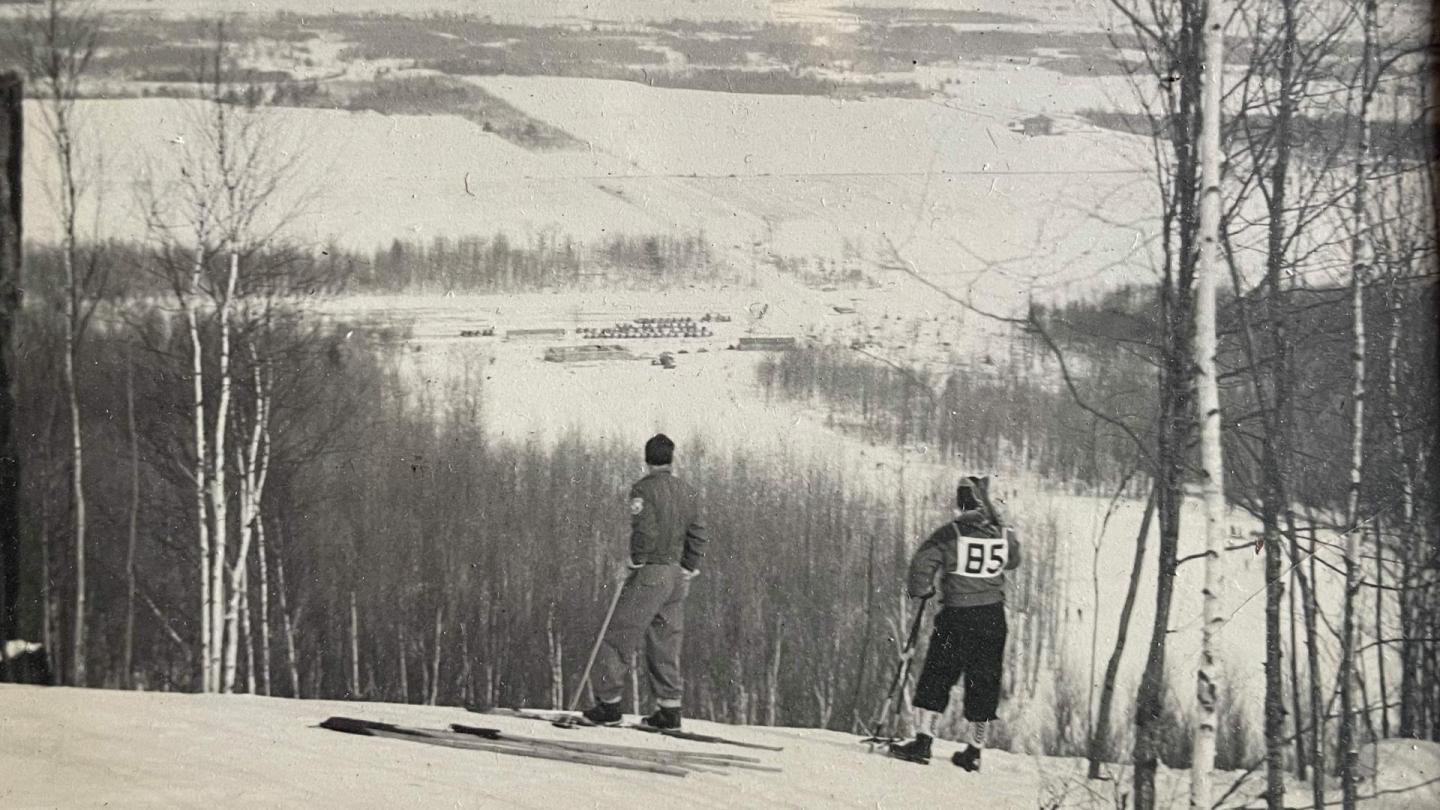 Two skiers on a snowy hill, overlooking a vast winter landscape.