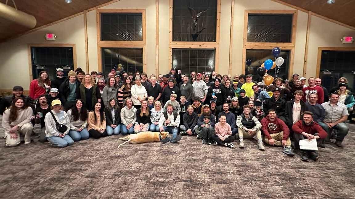 Large group of people posing in a spacious room with large windows.