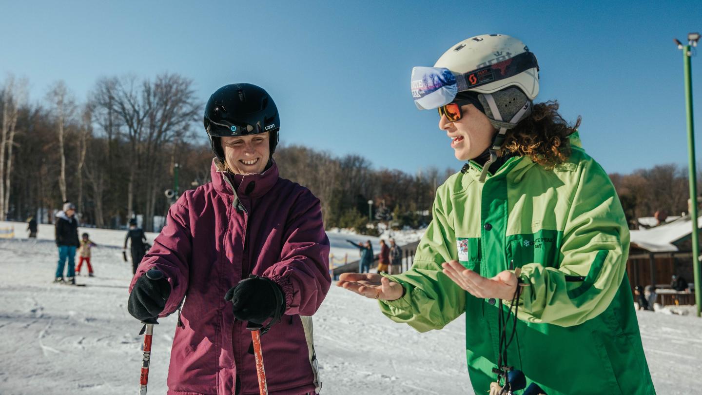 Ski instructor and student on snowy slope, wearing helmets and jackets.