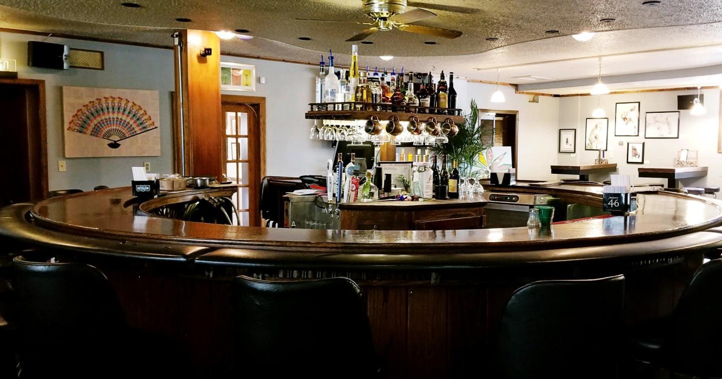 Cozy bar with wooden counter, stools, and stocked shelves.