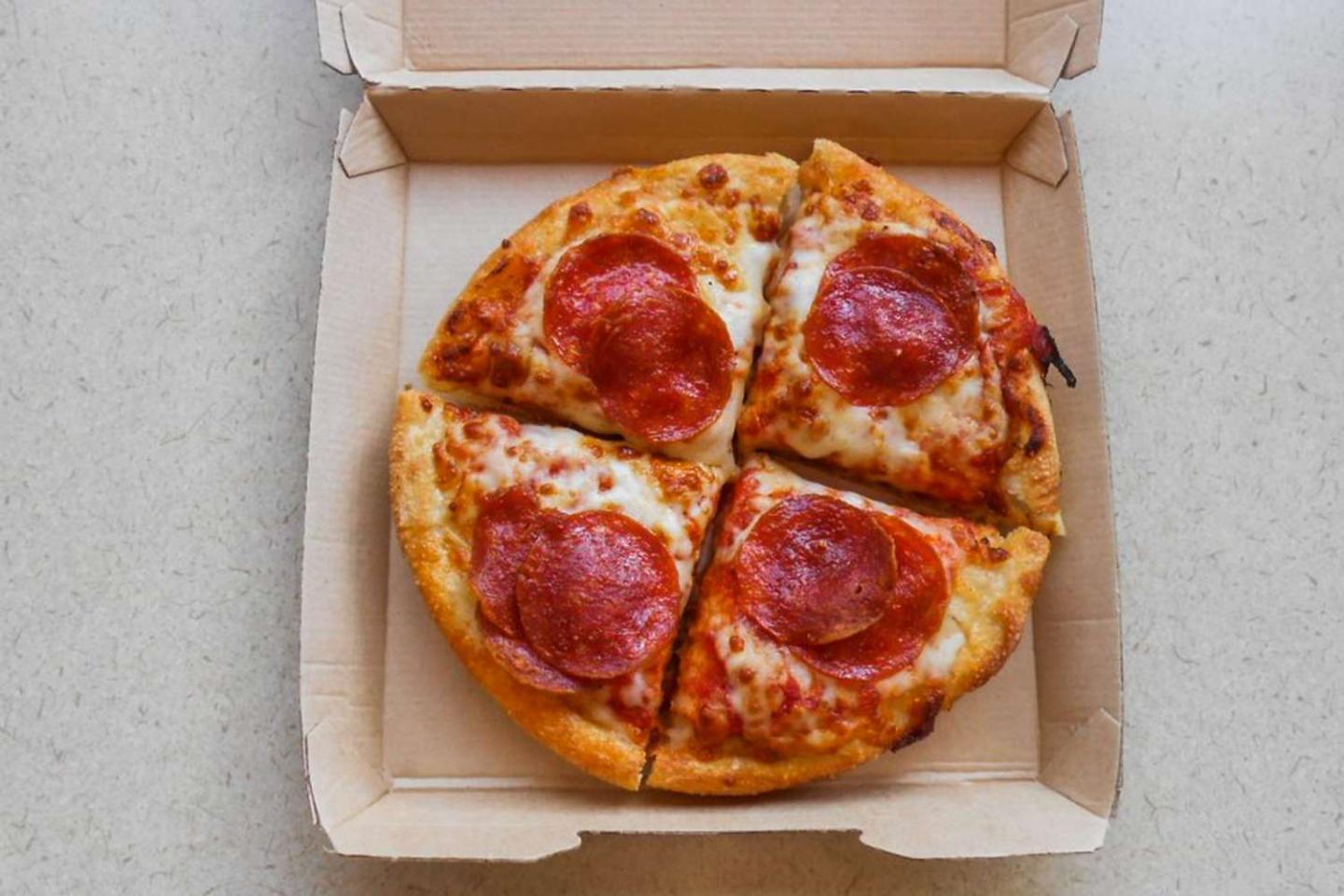 Pepperoni pizza in an open cardboard box, cut into four slices.