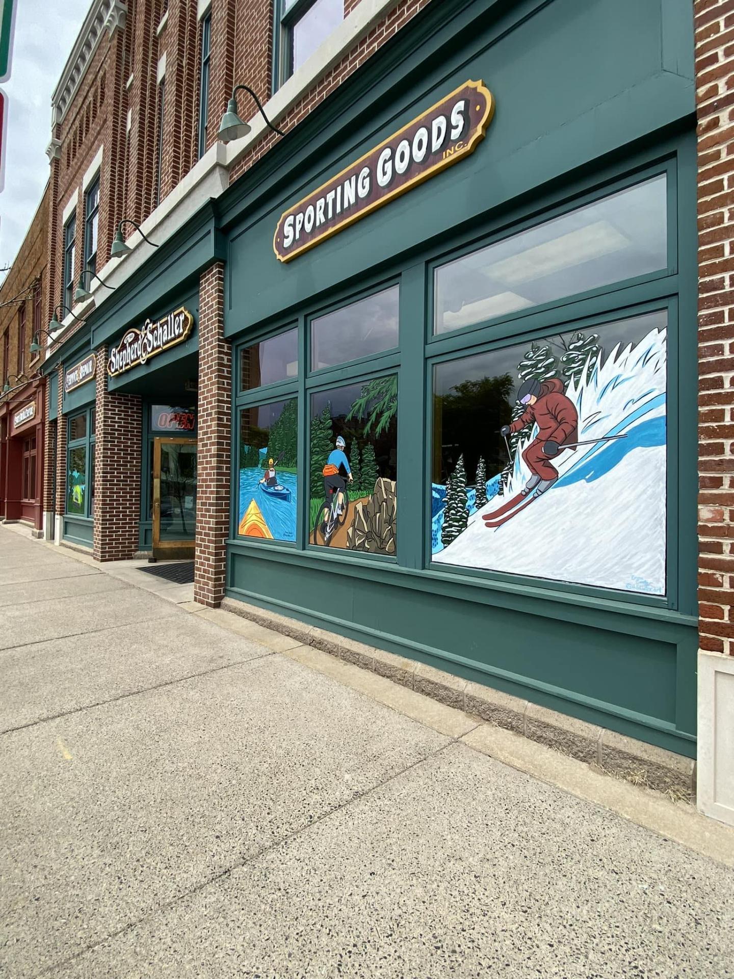 Storefront with sporting goods mural, brick facade, sidewalk view.