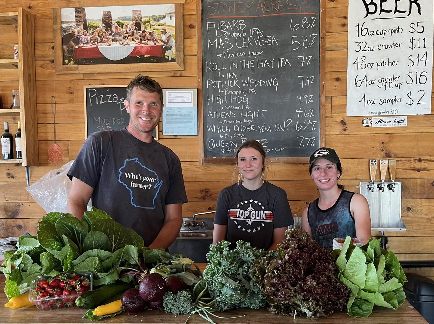 Three people behind a market counter with fresh vegetables.