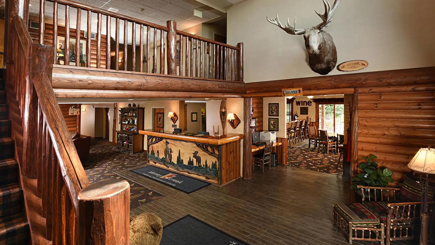 Rustic lodge lobby with wooden decor and mounted moose head above reception desk.