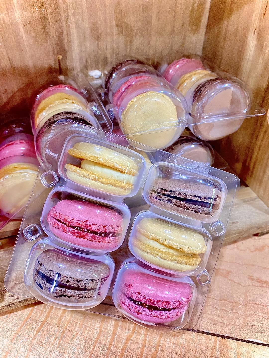 Pink and yellow macarons in clear plastic containers, placed on a wooden surface.