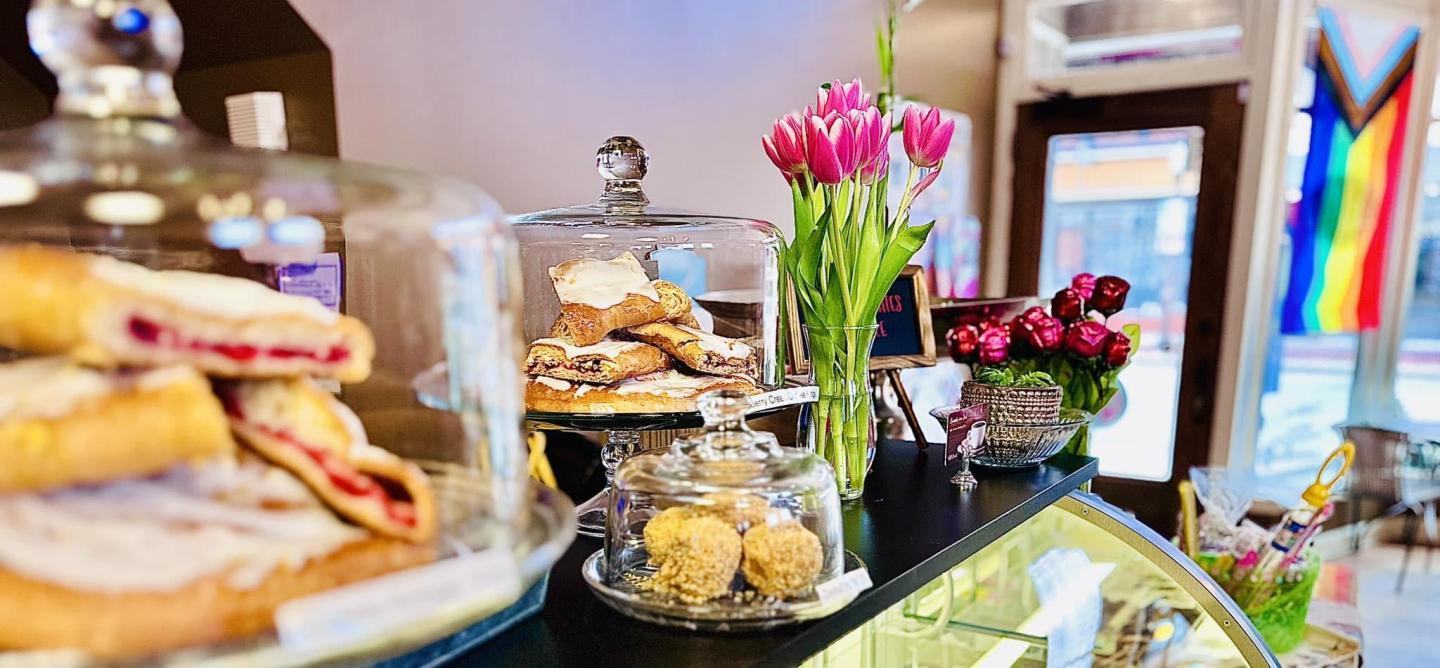 Bakery counter with pastries, pink tulips, and a rainbow flag.