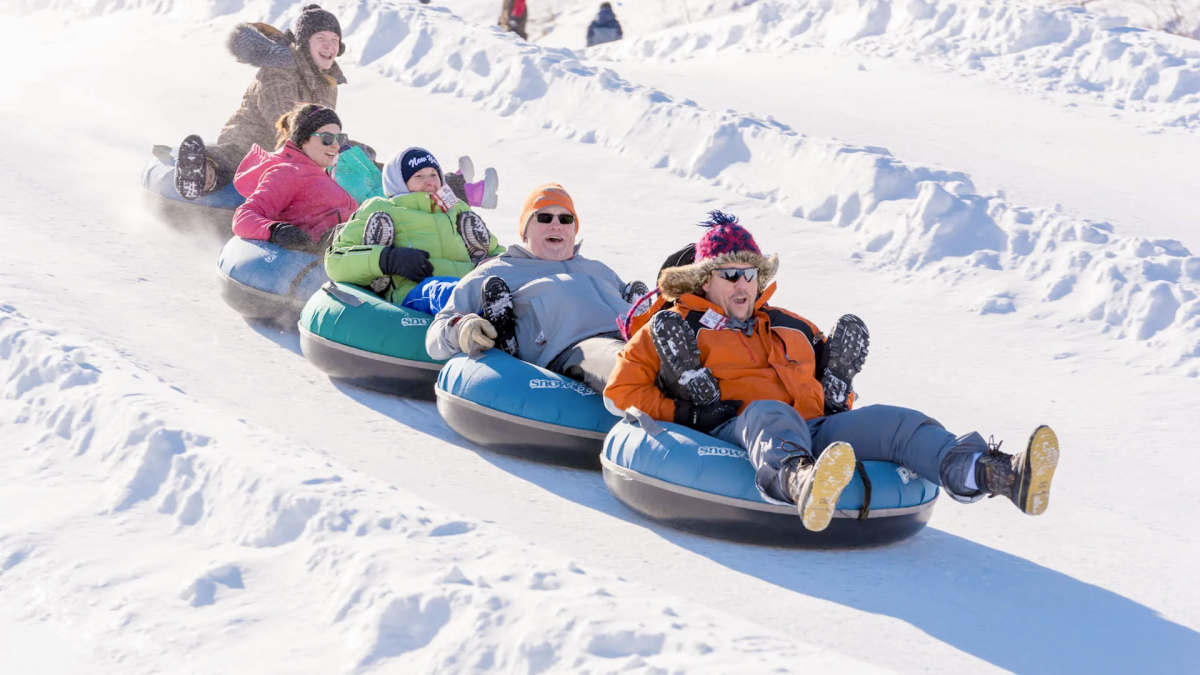 People tubing down snowy hill, wearing winter clothing and enjoying the ride.