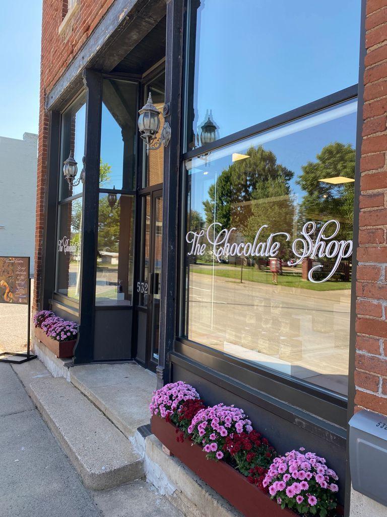 Brick storefront with large windows, pink flowers in boxes.