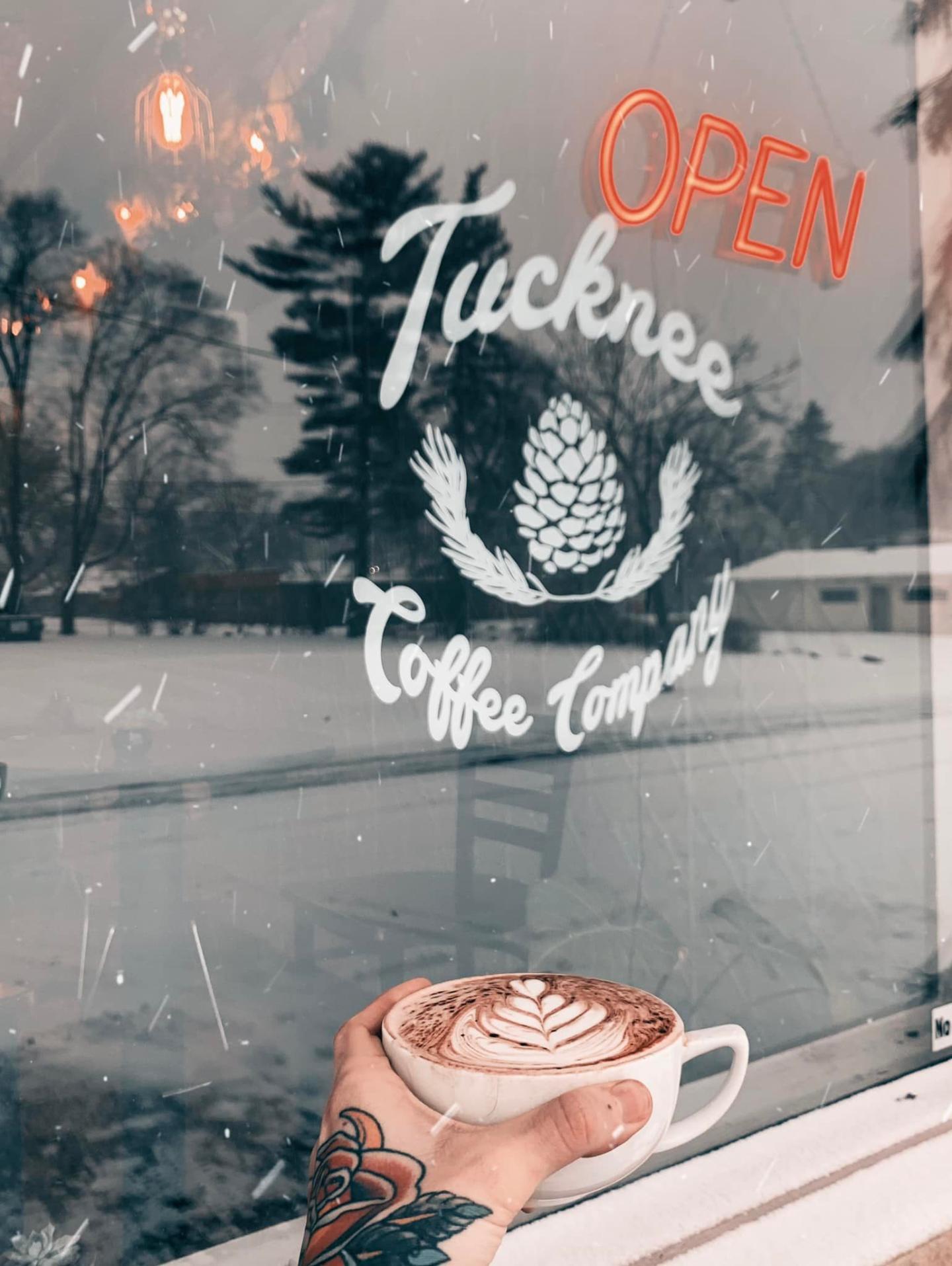 Hand holding a latte by a snowy window with a café logo.