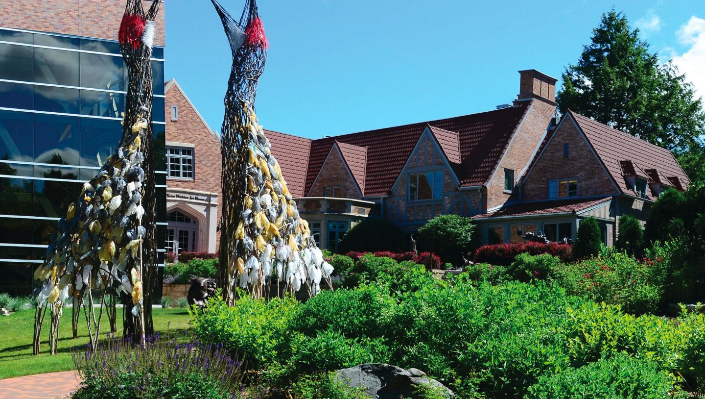 Brick building with sculptures and green gardens in sunny weather.