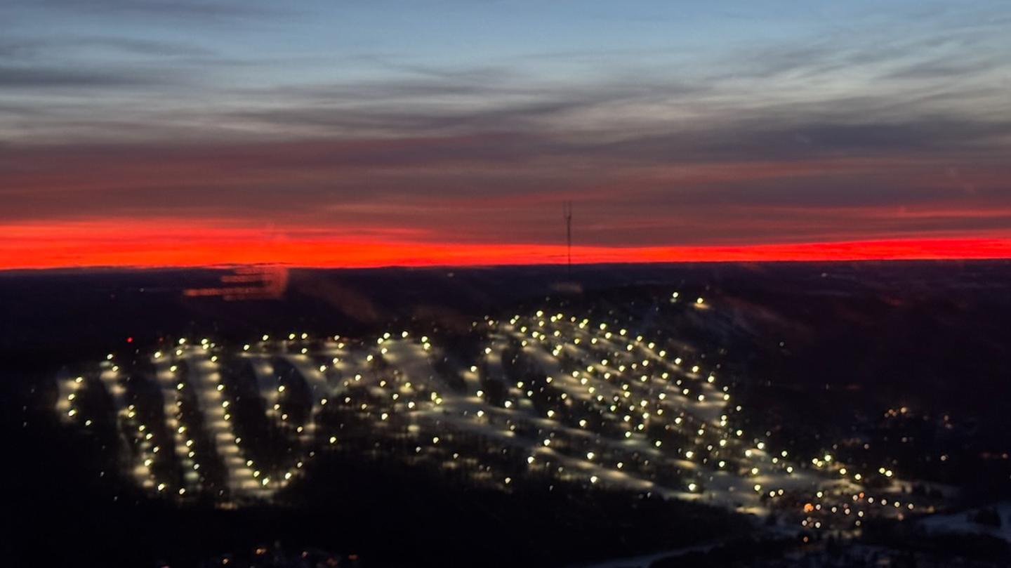 Ski resort lit up at night, against a vivid sunset with red and blue sky.