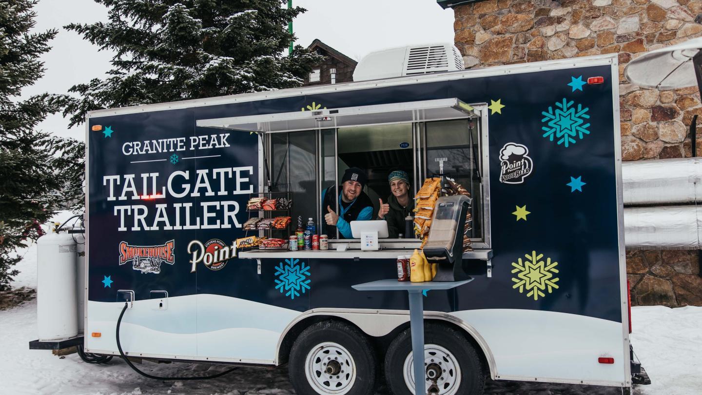 Food truck in snowy setting with two people serving inside.