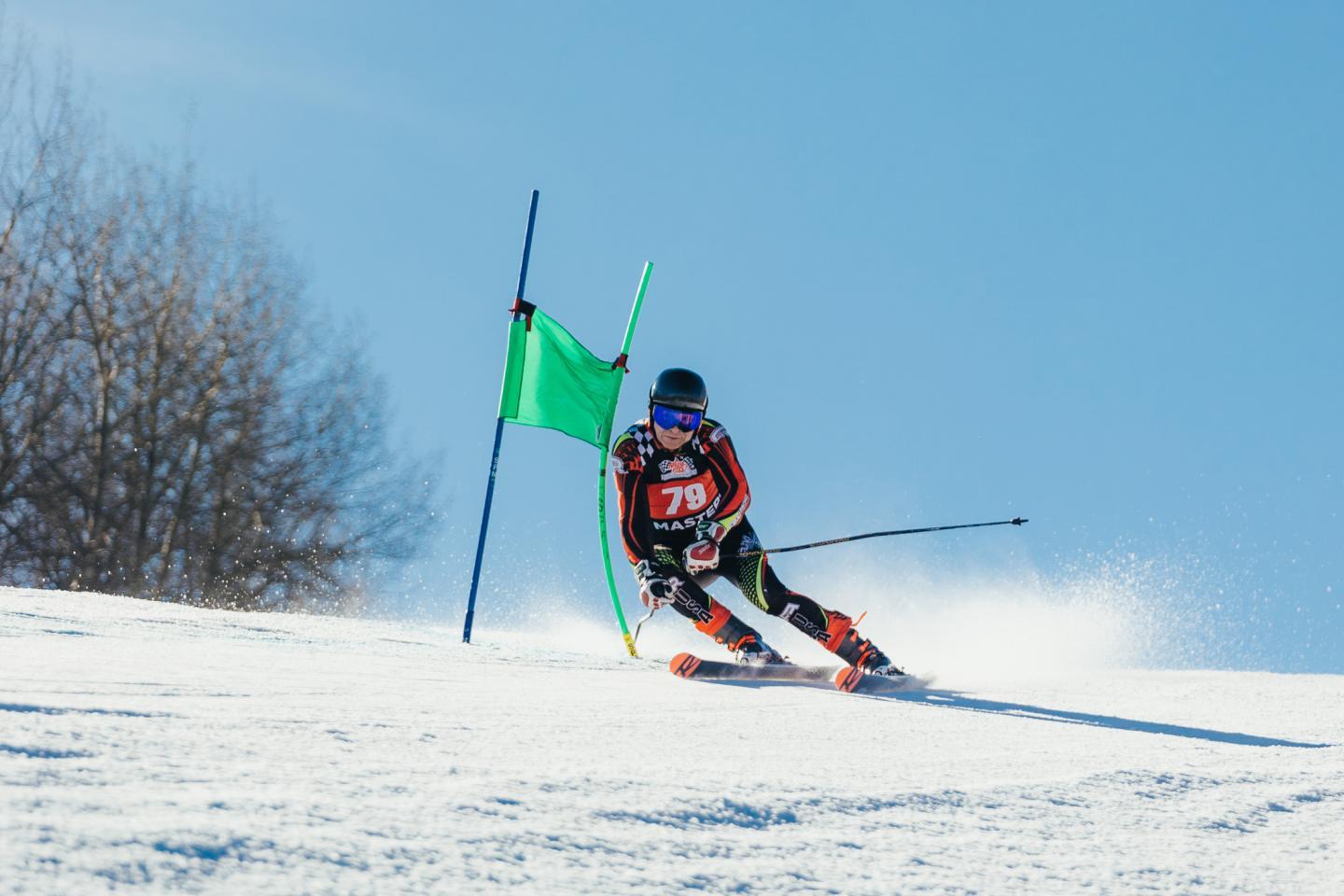 Skier racing downhill past green flag on snowy slope.