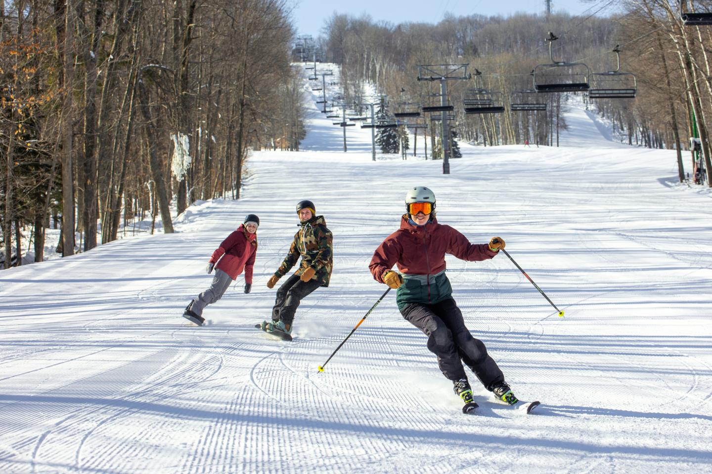 Three people skiing downhill on a snowy, tree-lined slope.