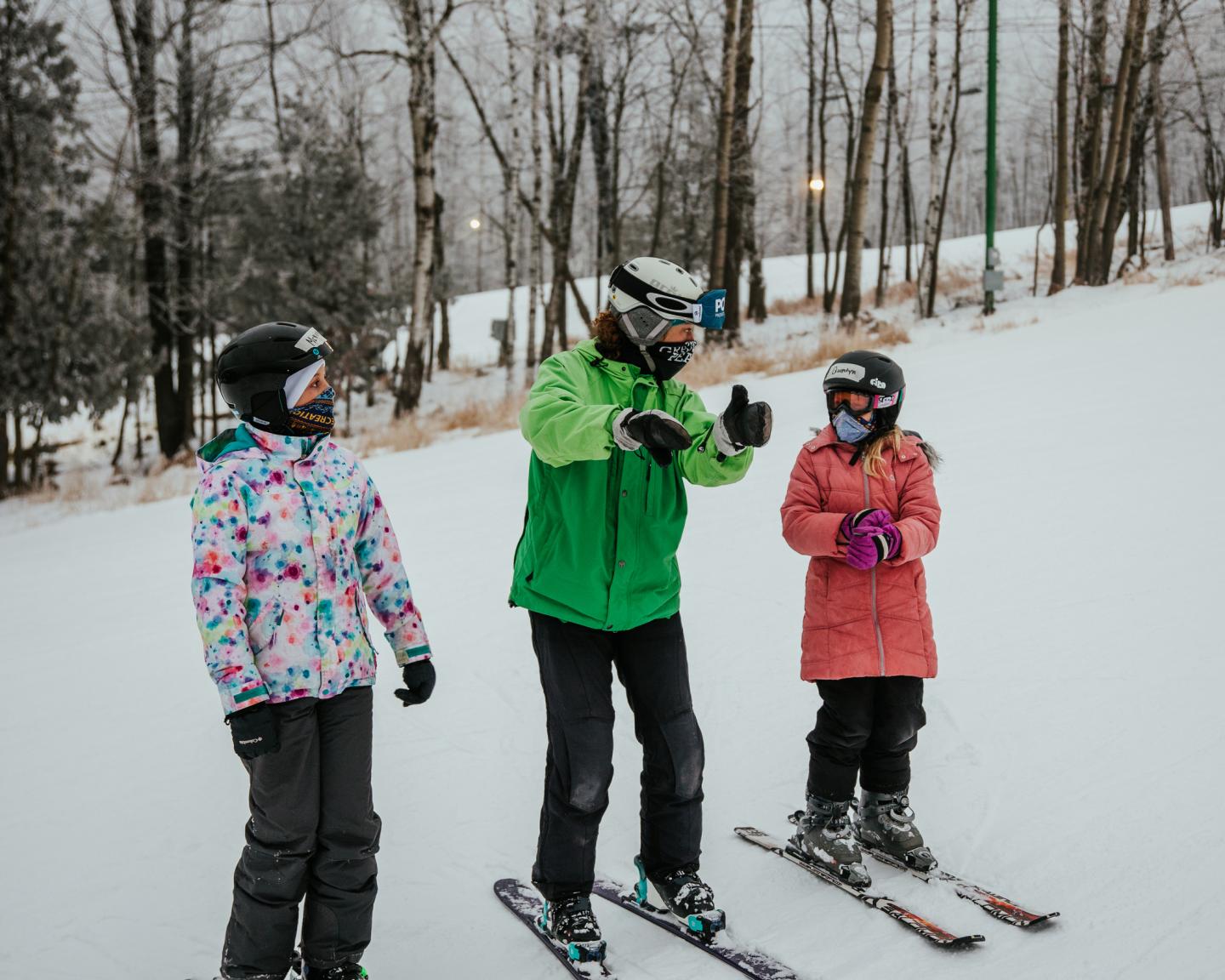 Three skiers on snowy slope, one giving instructions.