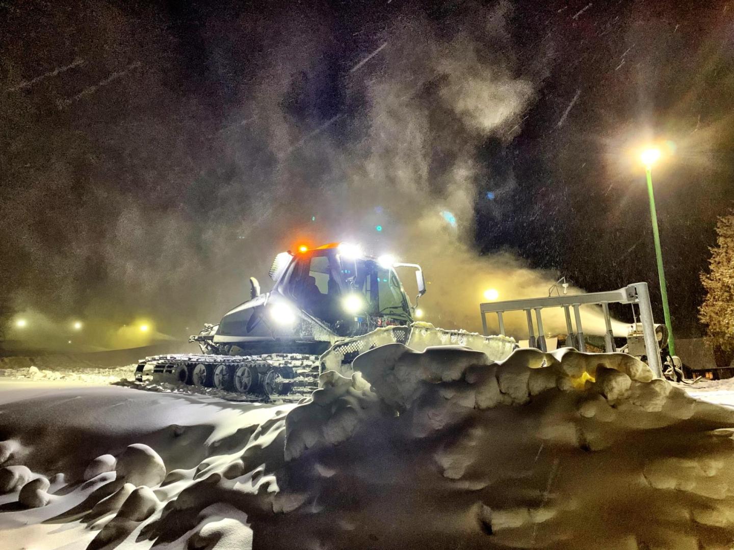 Snowplow clearing snow at night under streetlights.