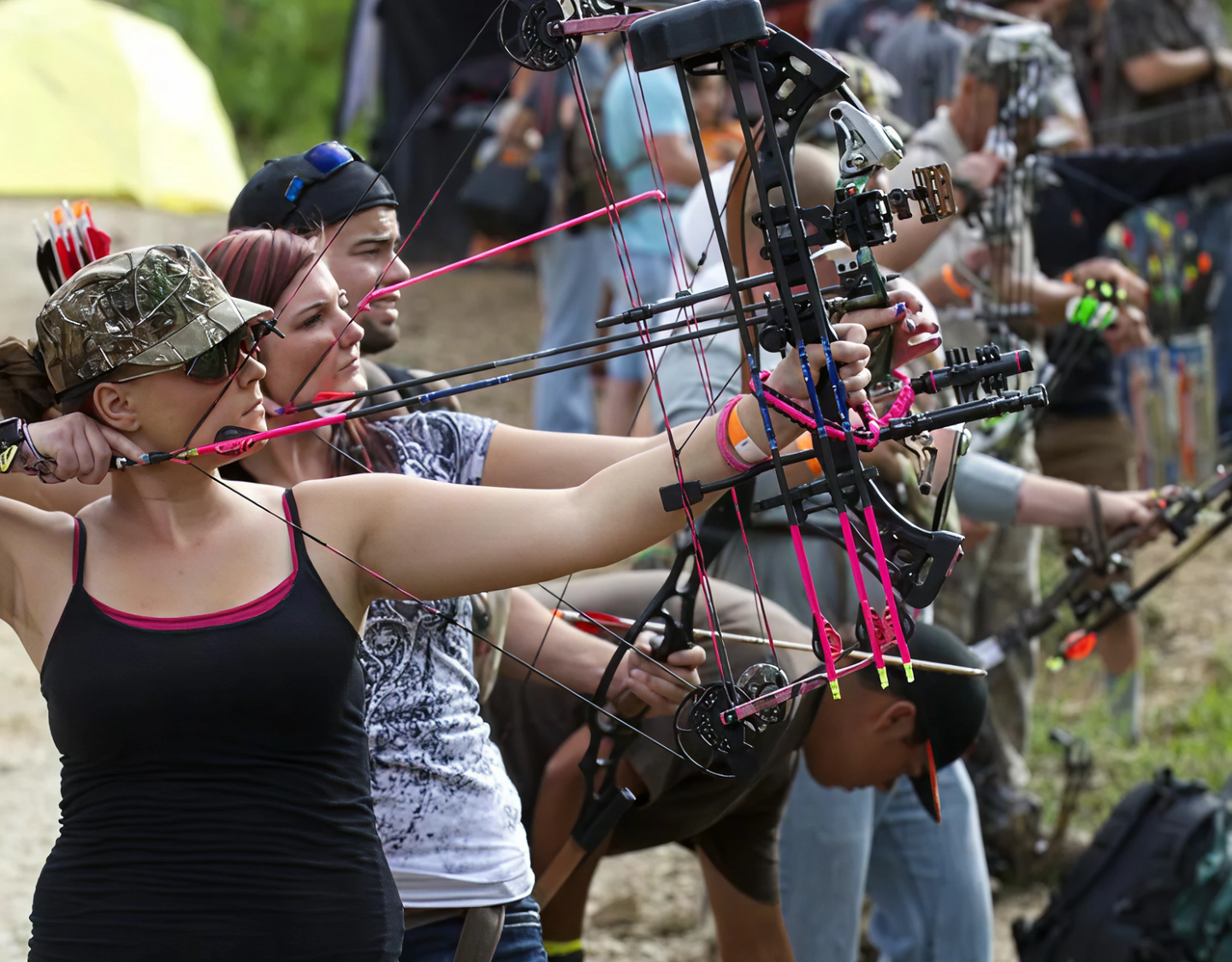 People aiming compound bows in an outdoor archery competition.