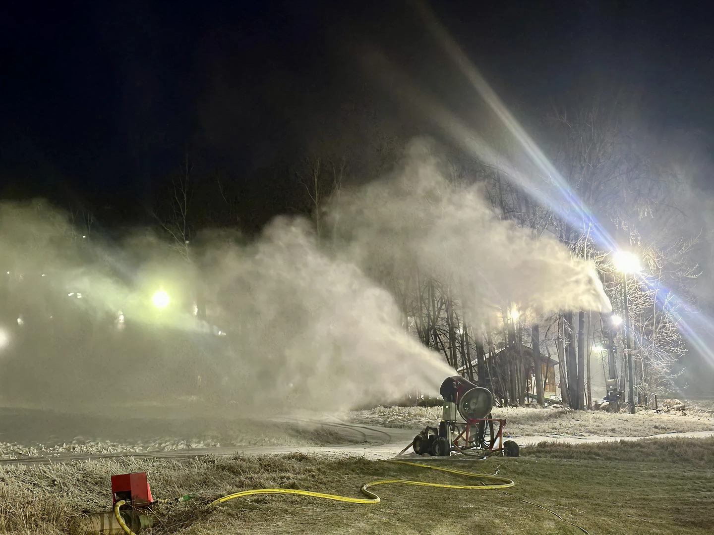 Snowmaking machine operating at night with bright lights and mist.