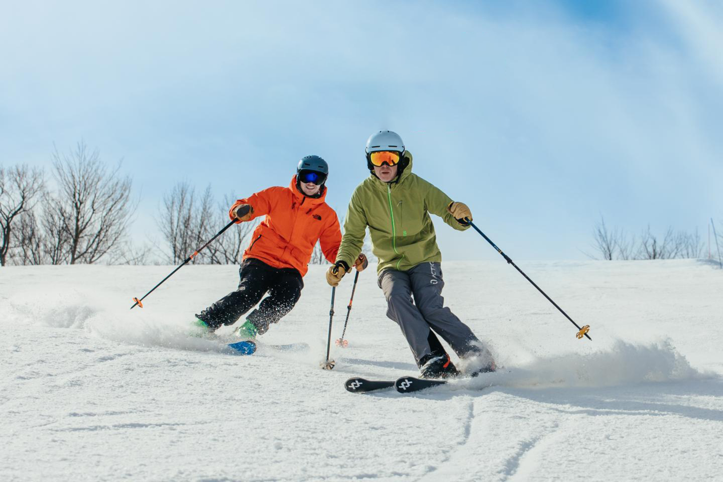Two skiers in colorful gear skiing down a snowy slope under a clear blue sky.