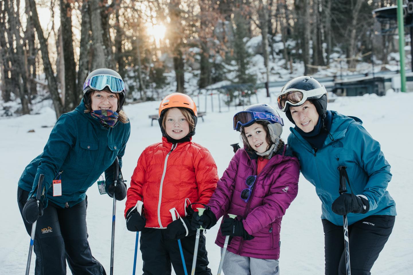 Four people in winter gear smiling, standing on a snowy ski slope.