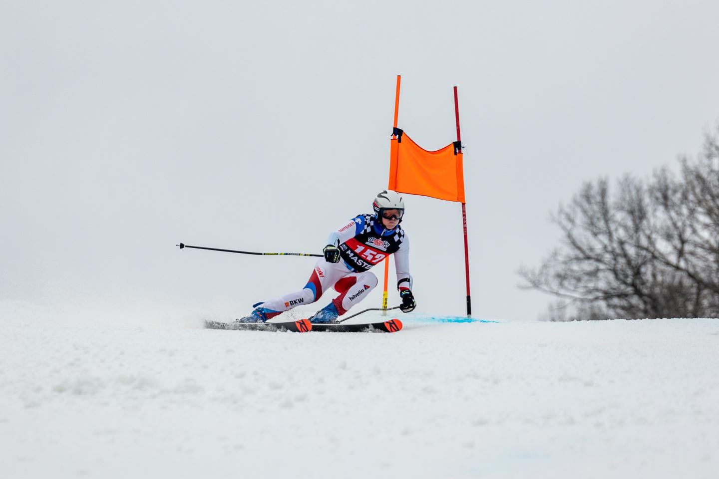 Skier in race suit navigating a slalom course, orange gate, snowy backdrop.