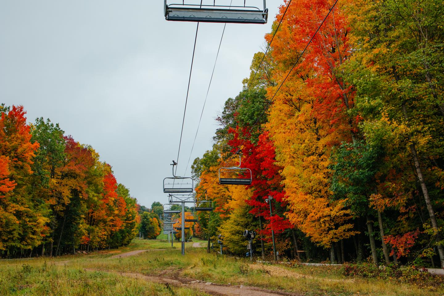 Chairlift over a path flanked by vibrant autumn trees.