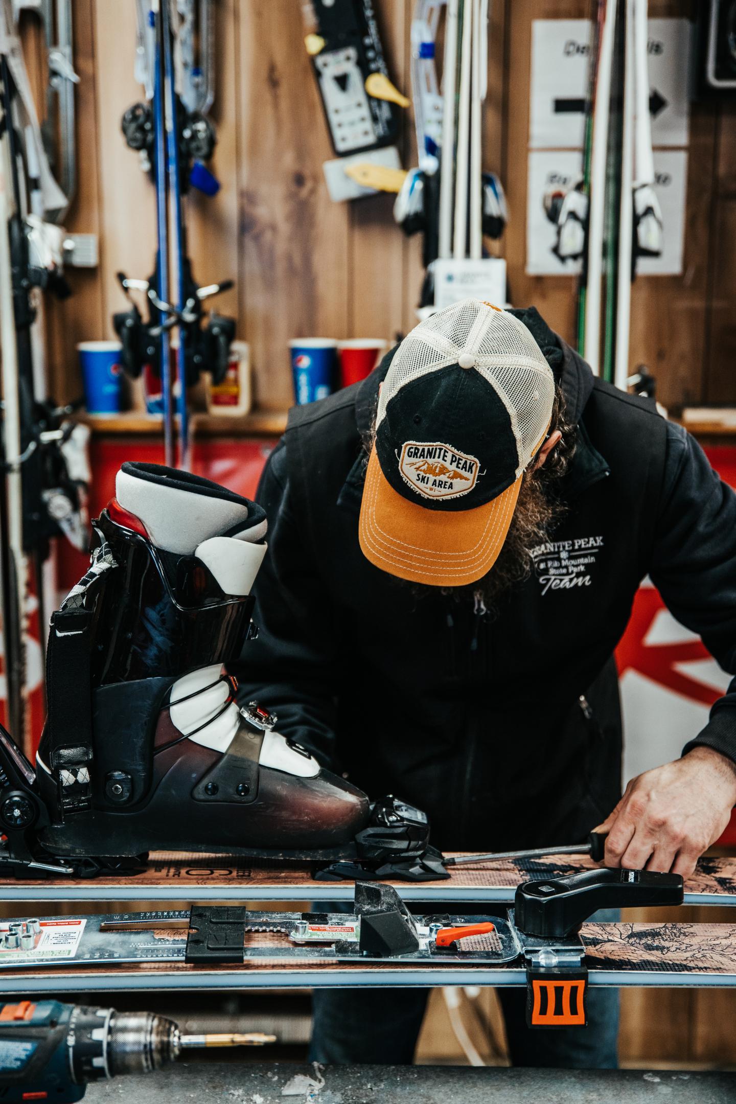Person adjusting ski bindings on a workbench in a ski shop.