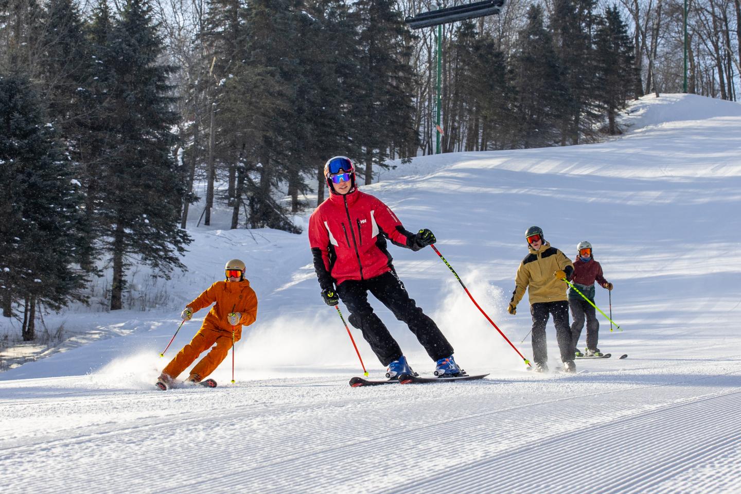 Skiers descending a snowy slope, surrounded by trees.
