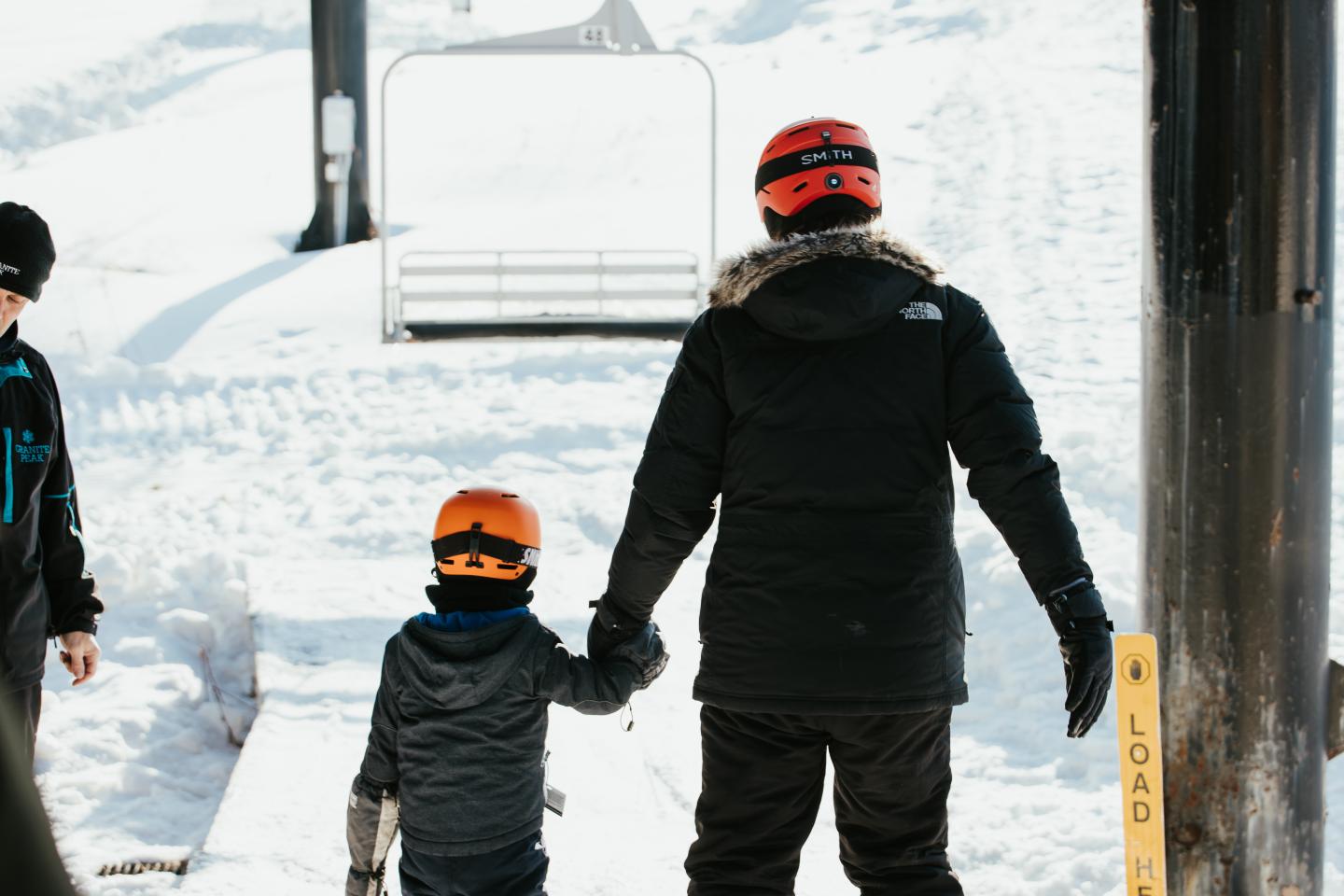 Adult and child in ski gear holding hands near a ski lift.