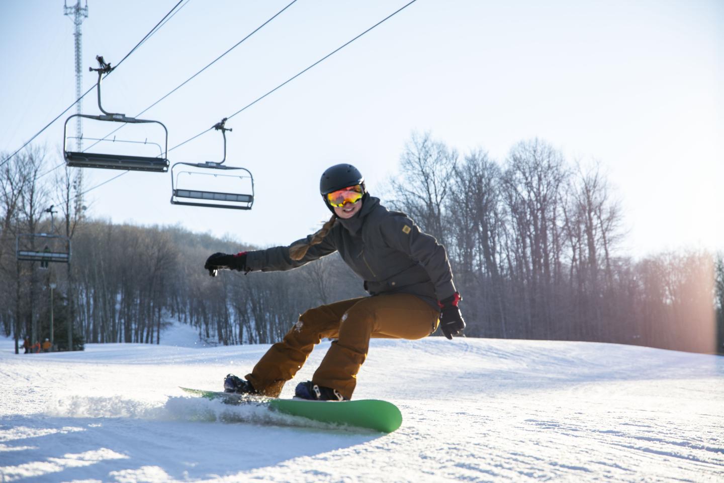 Snowboarder gliding down a sunlit slope under a ski lift.